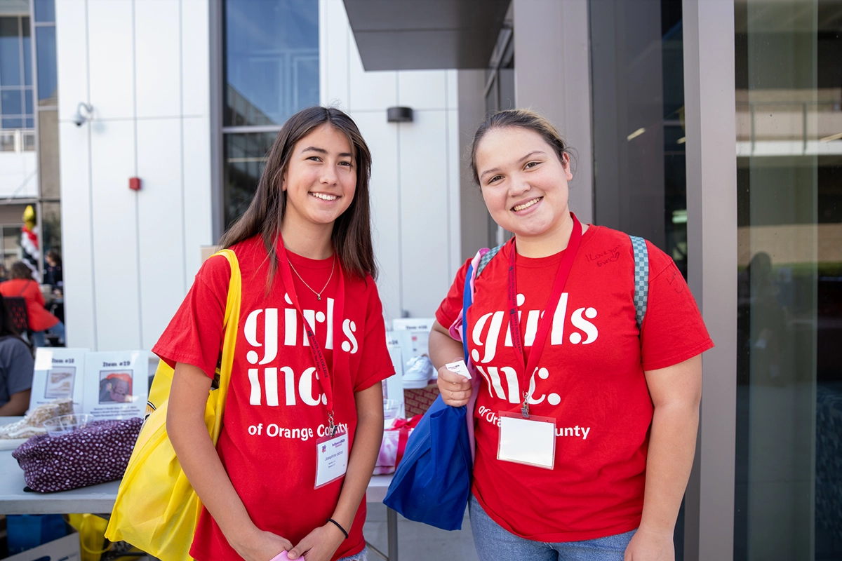 two-girls-smiling-standing-with-badges-and-tote-bags